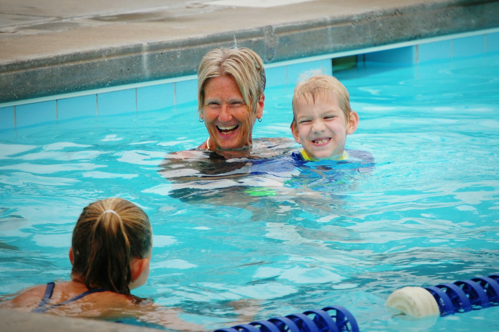 Three people are laughing and swimming together in a pool.