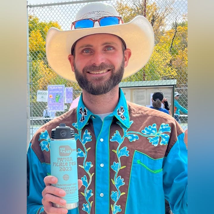 Man with a cowboy hat and teal shirt holding a "1st Place" water bottle from the "Peonia Pickle Fest 2023".