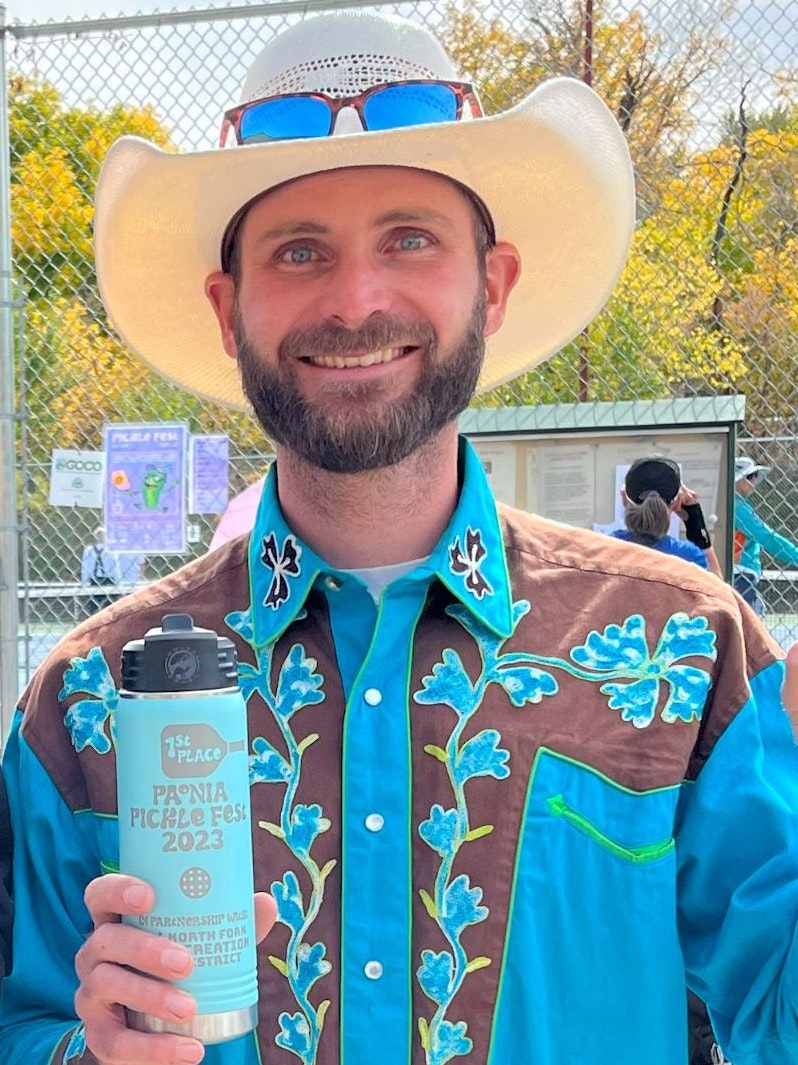 Man with a cowboy hat and teal shirt holding a "1st Place" water bottle from the "Peonia Pickle Fest 2023".