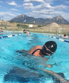 Swimmer in a cap in an outdoor pool with mountains in the background.