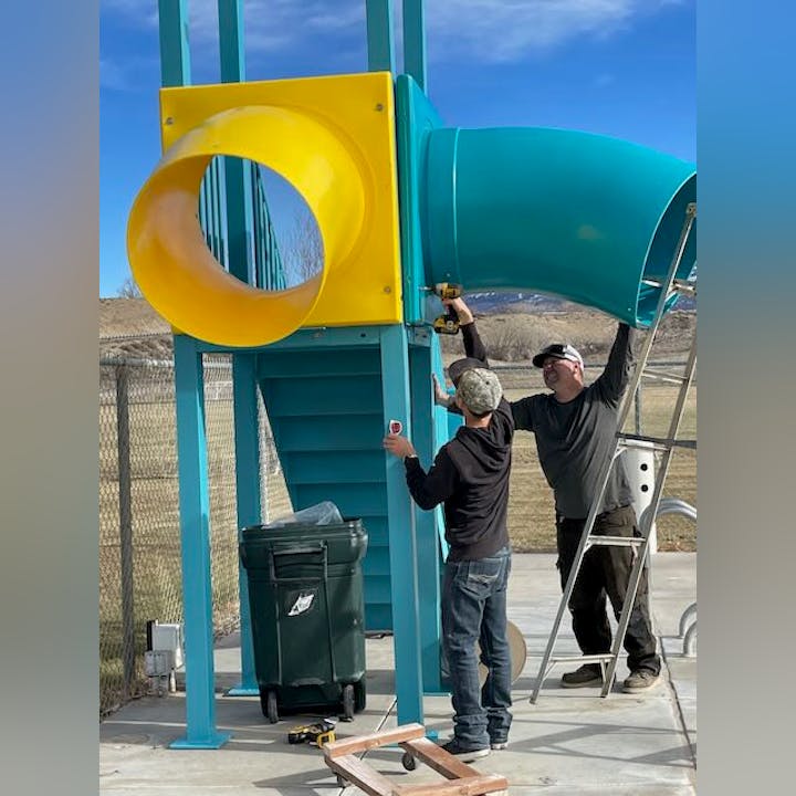 Two people assembling a playground slide outdoors.