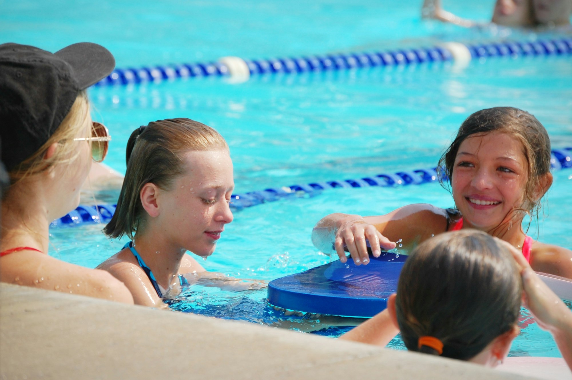 Kids in a swimming pool, smiling and using a kickboard.