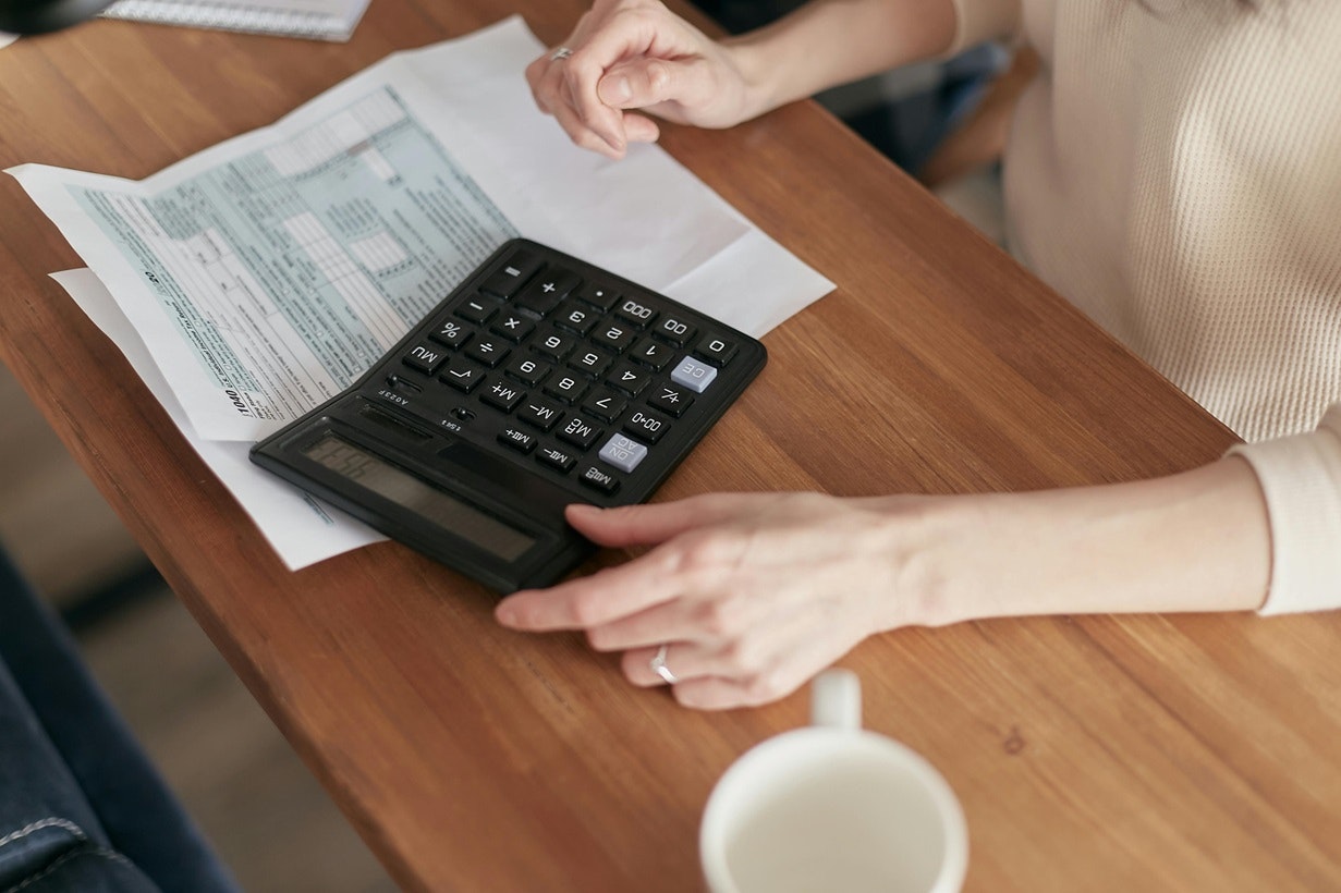 Person using a calculator and reviewing documents at a wooden table with a coffee cup.