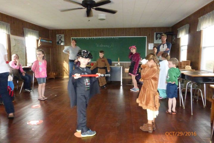 Children in costumes gather in a cozy room for activities, with one child dressed as a character holding a lightsaber.