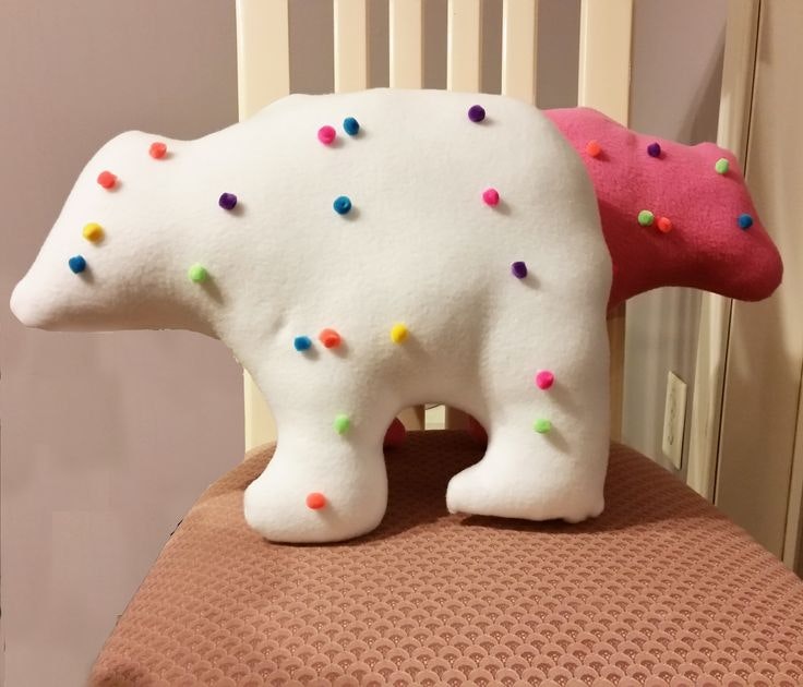 Plush bear-shaped cushions with colorful pom-poms on a chair.