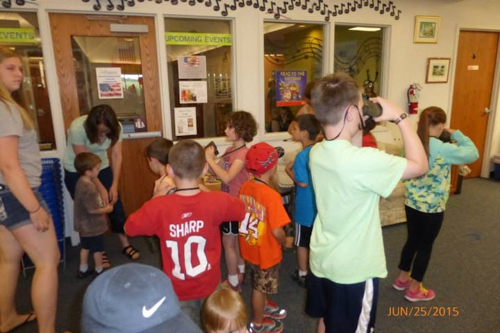A group of children in a library or community center, engaged in an activity, with adults supervising.