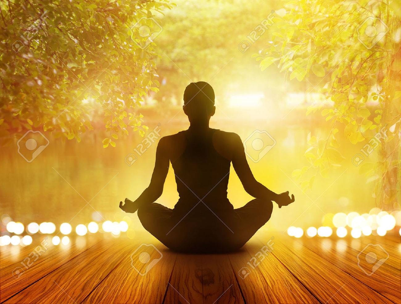 A silhouette of a person meditating in front of a calming, illuminated natural background.