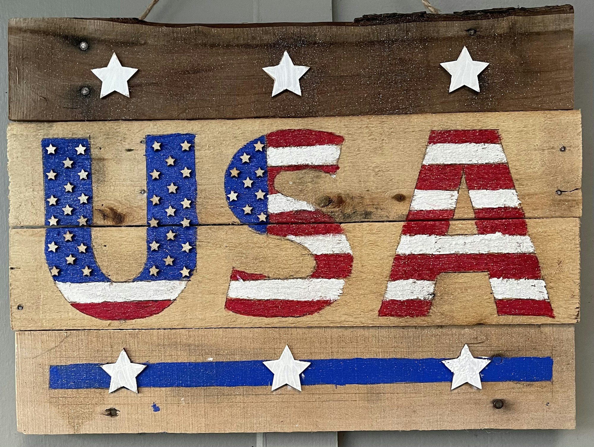 Rustic wooden sign with "USA" painted like the American flag and decorative stars.