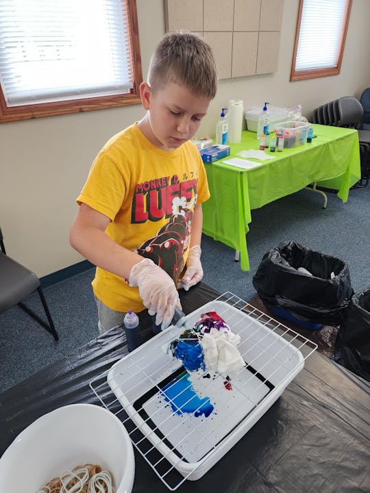 A boy making a tie-dye shirt on a rack with gloves and dye bottles.