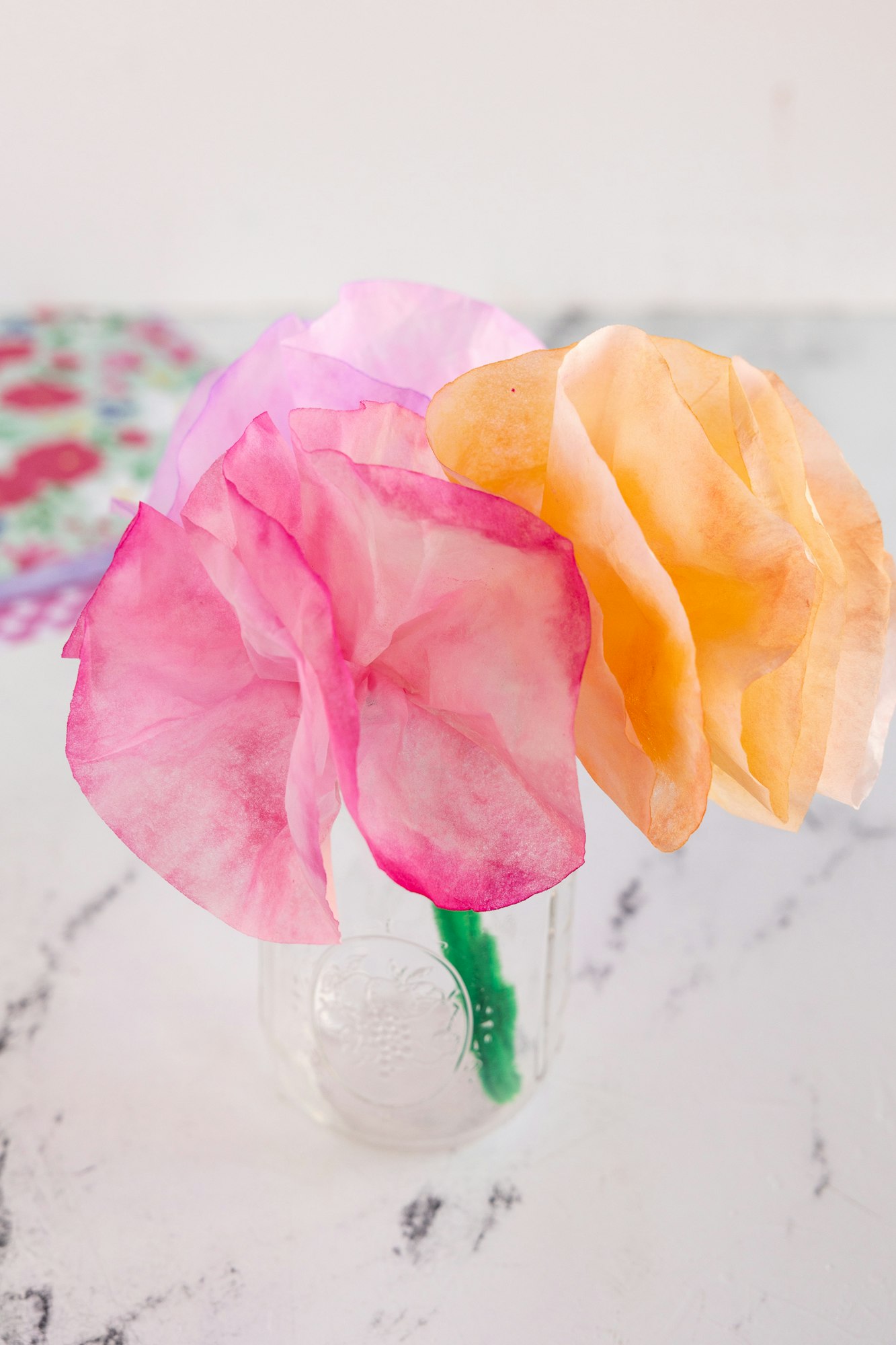 The image features colorful tissue paper flowers arranged in a clear jar.