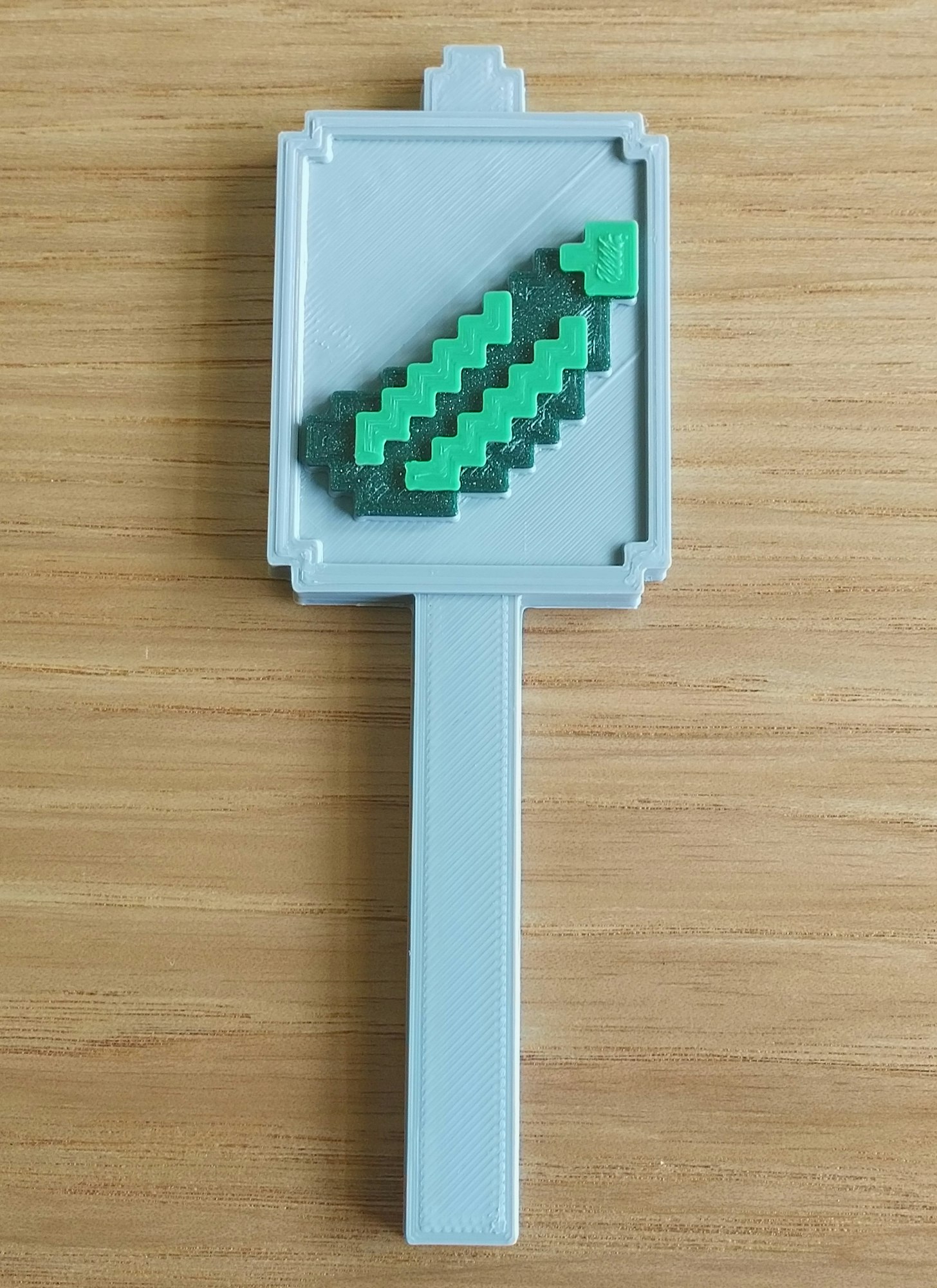 A 3D-printed Minecraft cookie cutter shaped like a pickaxe, placed on a wooden surface.