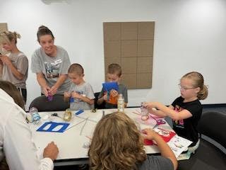 A group of children engaged in craft activities with an adult supervising.