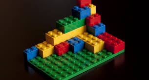 A colorful Lego structure with red, yellow, blue, and green bricks on a green baseplate.