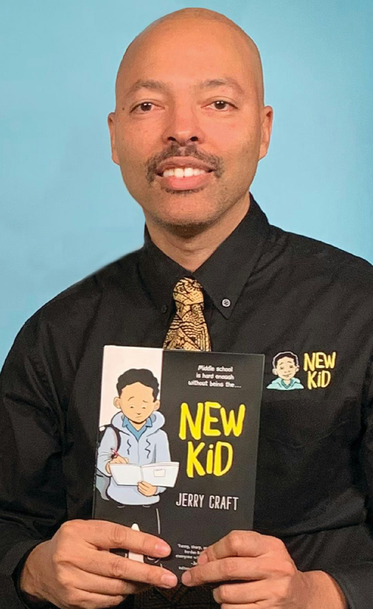 A person holds the book "New Kid" by Jerry Craft, wearing a matching shirt.