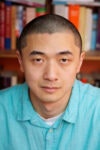 A person in a turquoise shirt is in front of a bookshelf filled with books.