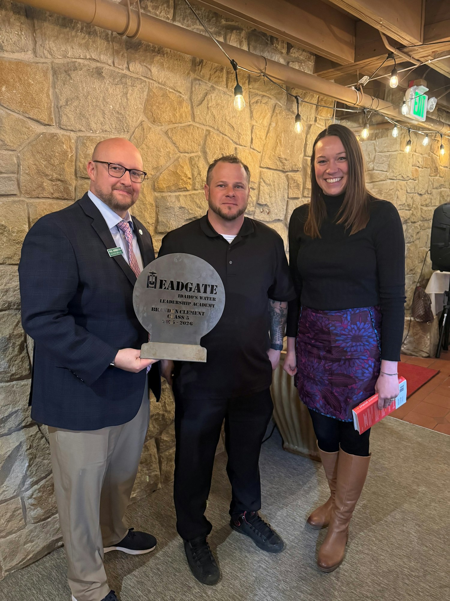 Three individuals pose with an award, celebrating a leadership achievement in a cozy, well-decorated venue.