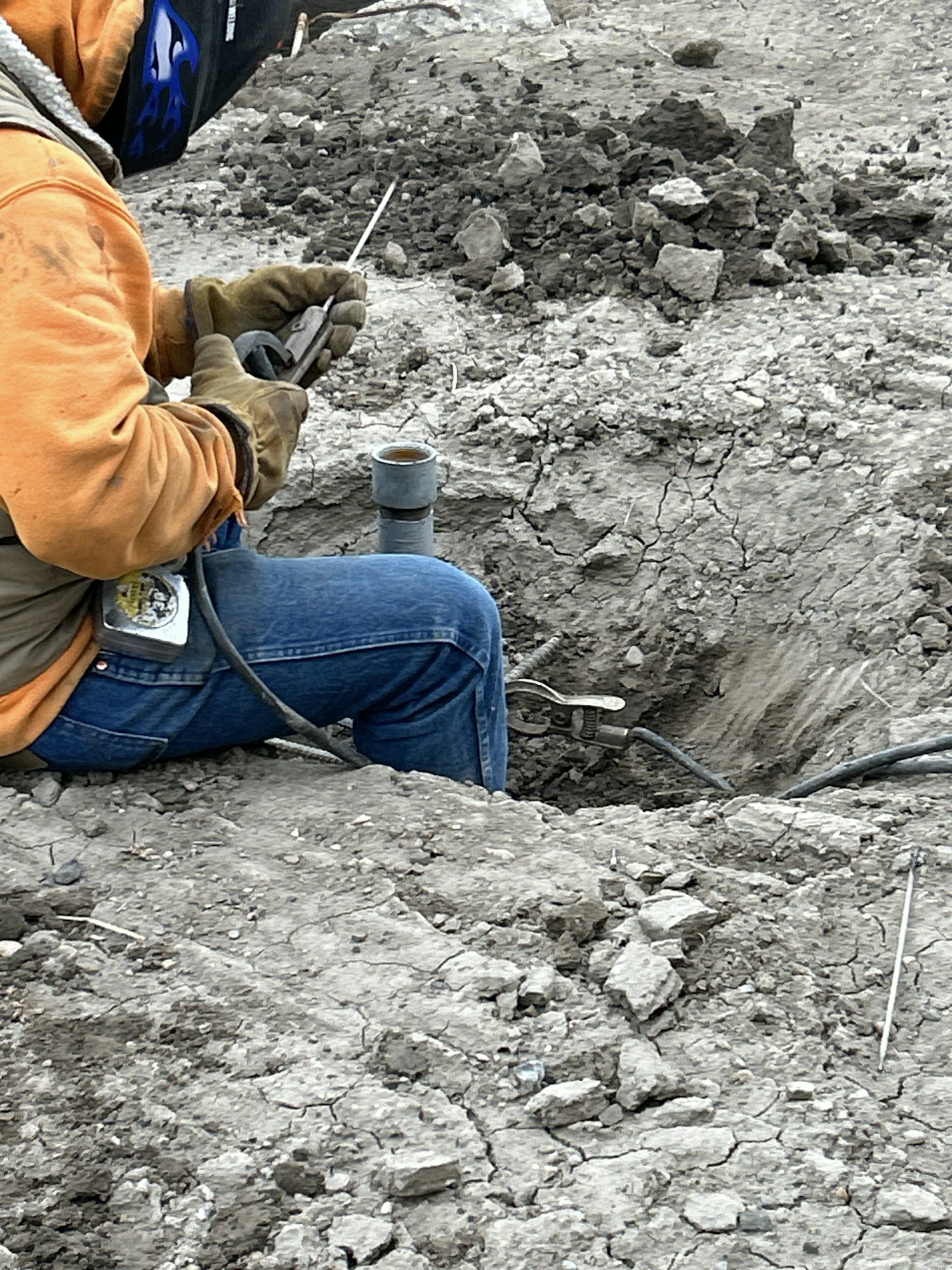 A worker in safety gear kneeling on rocky ground, handling tools and cables.