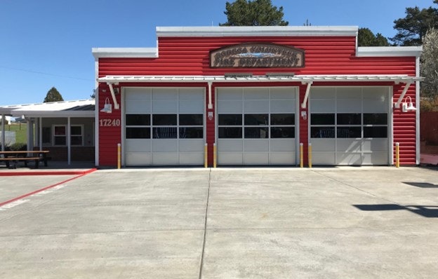 A red and white fire station with three garage doors and a clear sky.