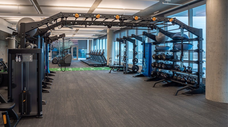 A modern gym with exercise machines, weights, and large windows.