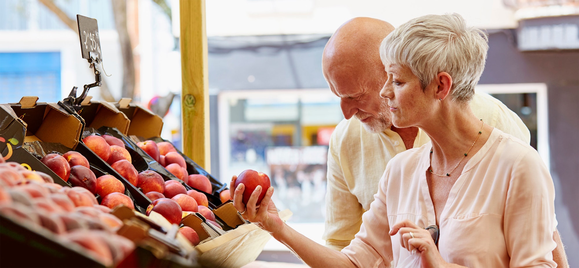 A couple is selecting nectarines at an outdoor fruit market stall.