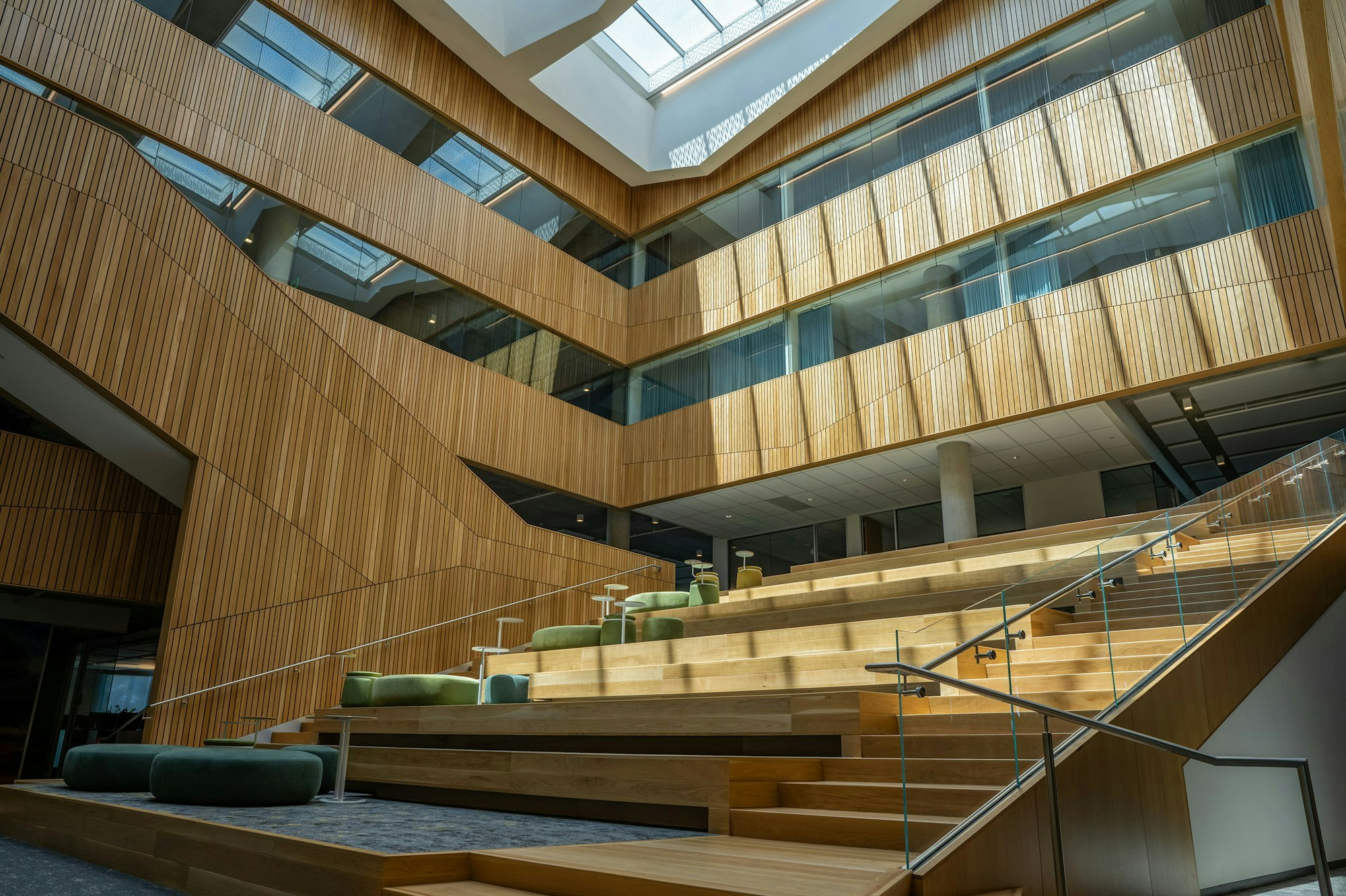 Modern interior with wooden stairs, seating areas, and sunlight through the skylight.
