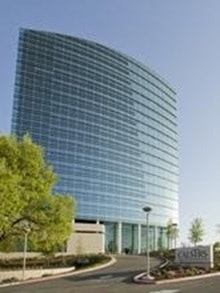 CalSTRS headquarters. A modern, curved glass building with surrounding greenery and a clear blue sky.