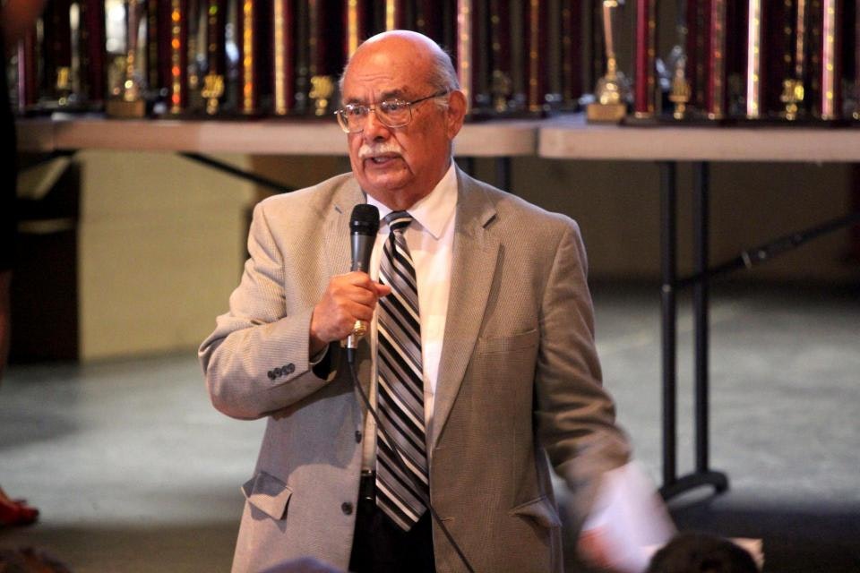 Joe Mendoza is wearing a suit and tie and talks into a microphone.