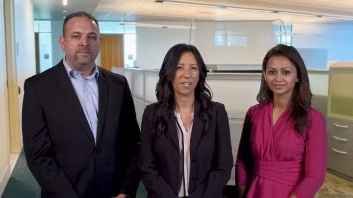Three people standing in an office setting, smiling at the camera.