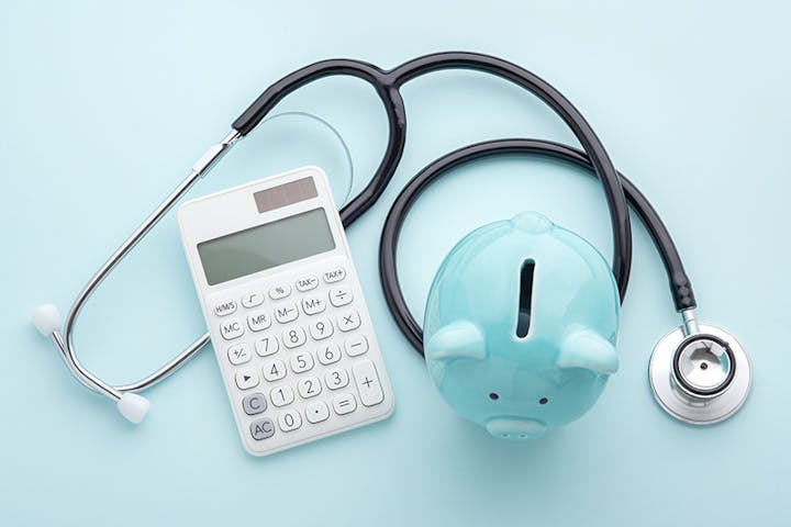 An image featuring a stethoscope, a calculator, and a piggy bank on a light blue background, symbolizing healthcare and finances.