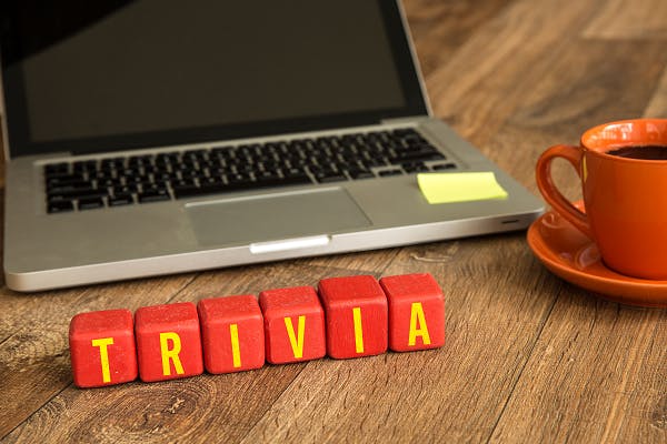 Laptop with sticky note, coffee cup, and blocks spelling "TRIVIA".