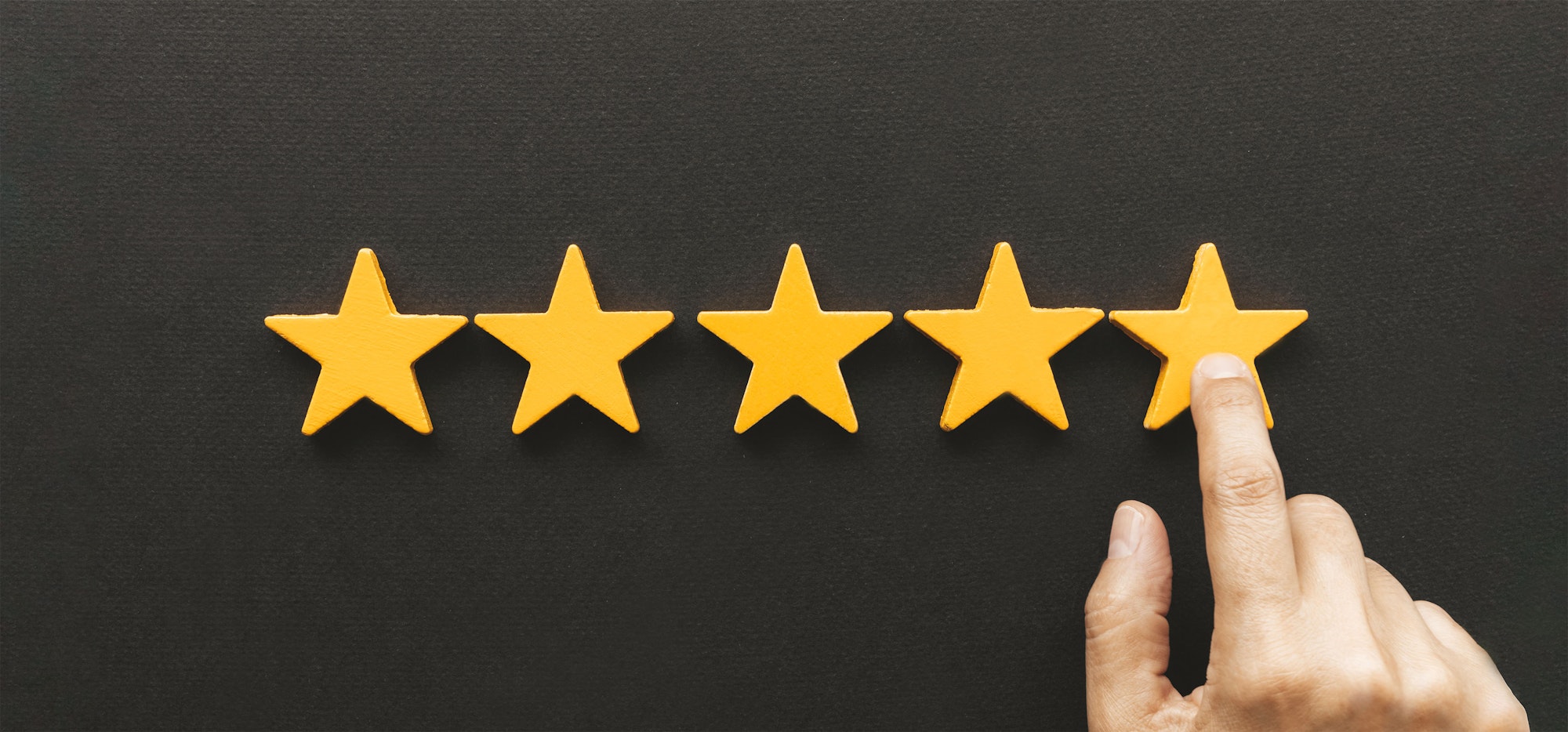 Five yellow stars on black background; finger touching the third star.
