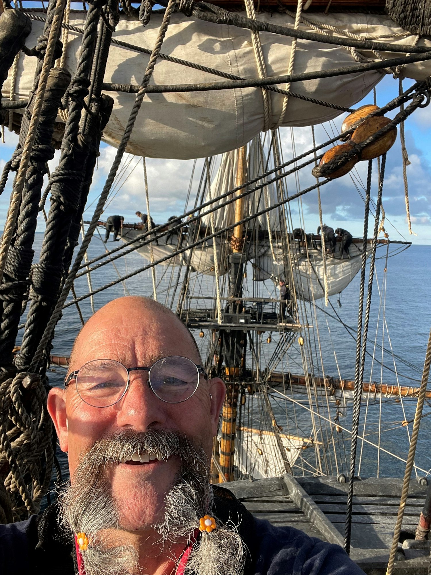 Mark Galipeau is bald and wears glasses. He has a long gray mustache. There are sails and water in the background.