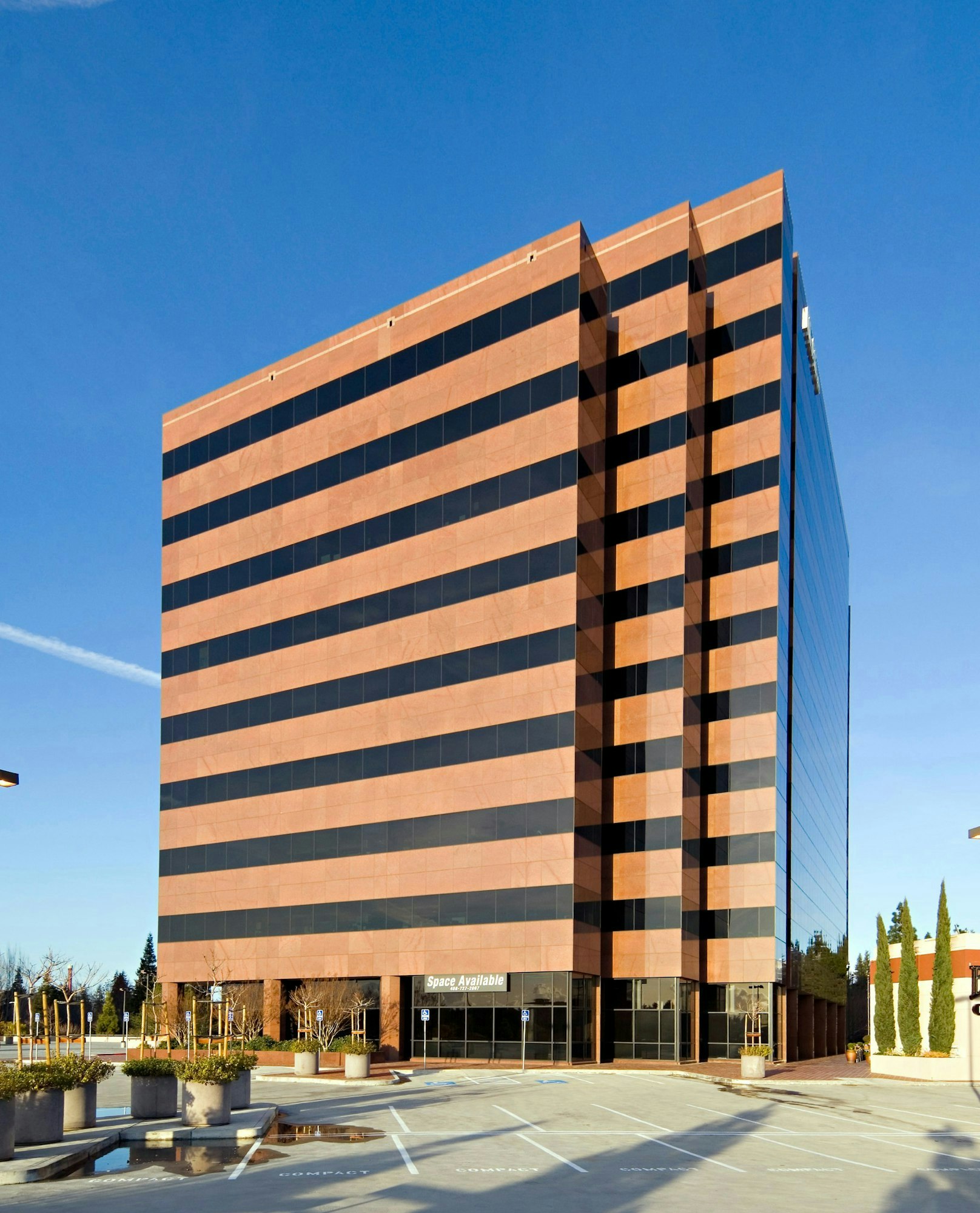 A modern office building with "Space Available" sign, clear sky, and an empty parking lot.