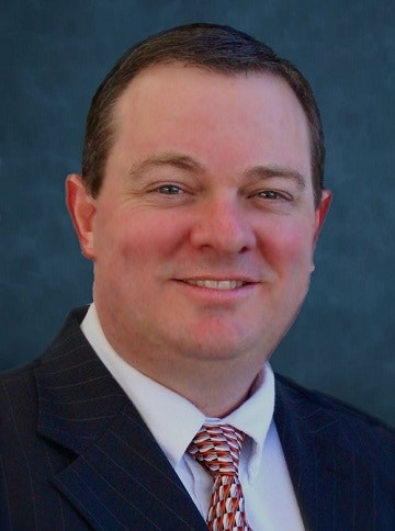 Aaron Ivey has short hair, wears a dark blazer and tie.
