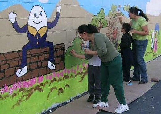 Adults and students painting a mural featuring Humpty Dumpty on a playground wall.