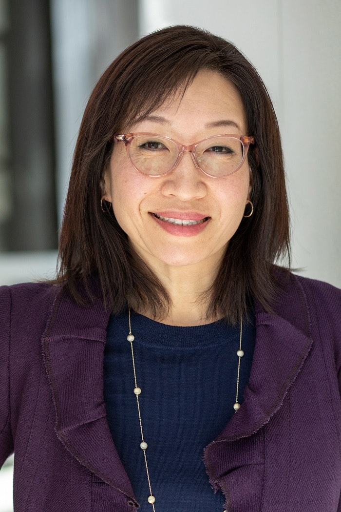 June Kim with glasses, wearing a purple jacket and a long necklace.