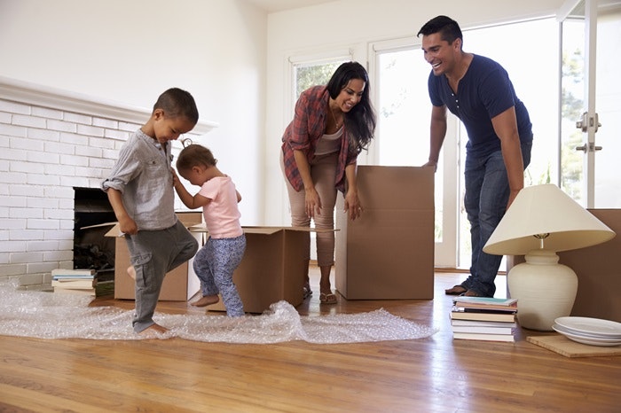 Family unpacking moving boxes, playing with bubble wrap in a bright room with a fireplace.
