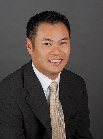 Anthony Chiu in a suit and tie is smiling against a gray background.