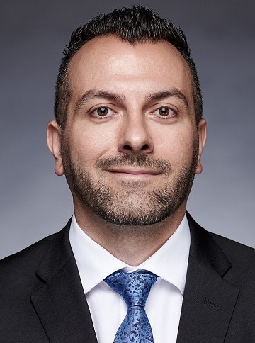Aren Yarian has short hair, wears a dark blazer and blue tie.
