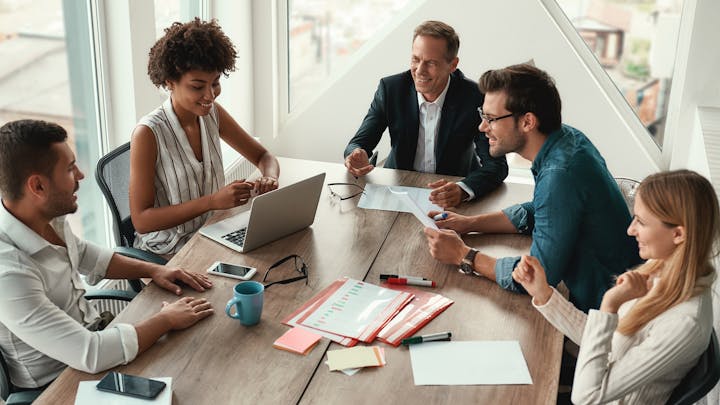 Group of young business people discussing something and smiling while sitting at the office table