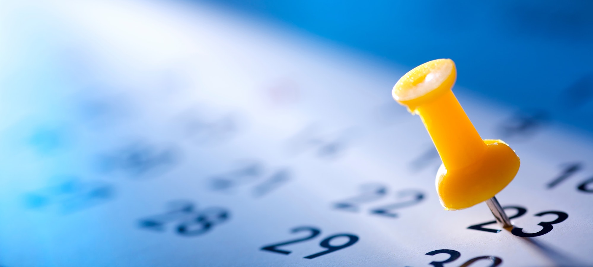 A close-up of a yellow pushpin on the 23rd day of a calendar.