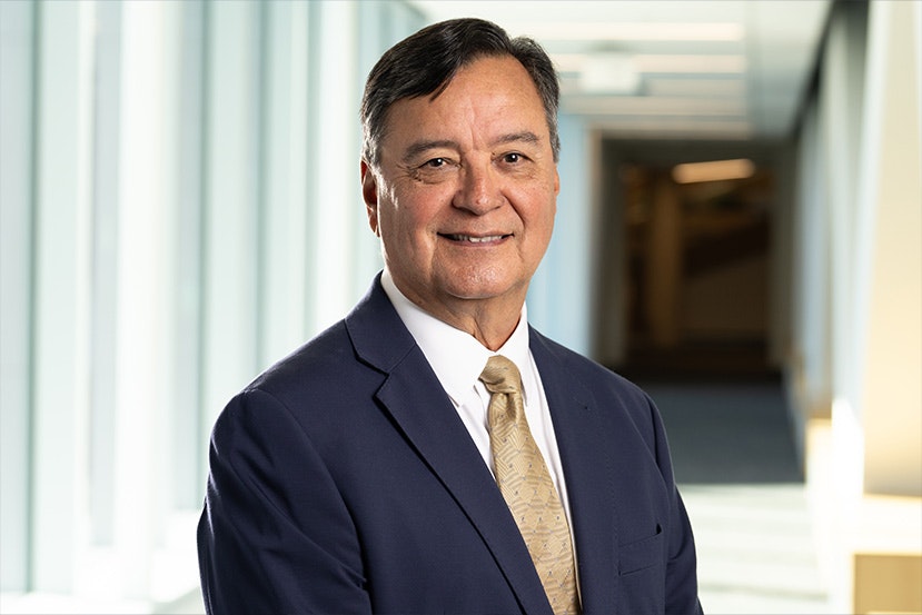 A man in a suit and tie smiling in a brightly lit hallway.