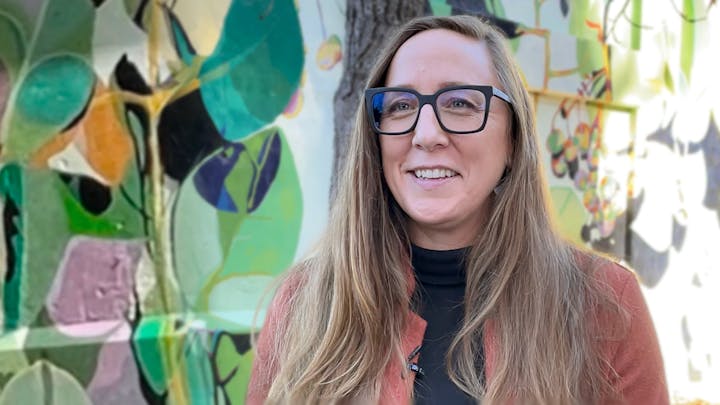 Lura Wilhelm smiles in front of a colorful mural.