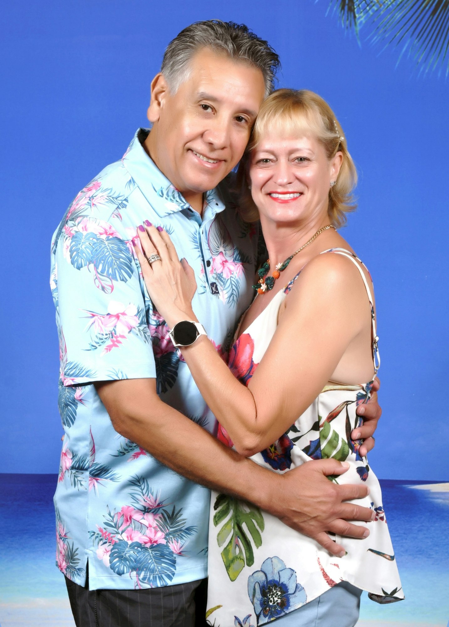 Kathy Cuevas is blonde and hugs her husband, who has graying hair. hey both wear colorful beach attire for their vacation.