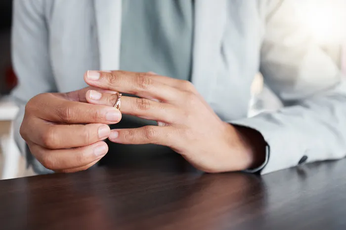 A person in a suit is removing a ring while sitting at a table, suggesting a moment of reflection or decision.