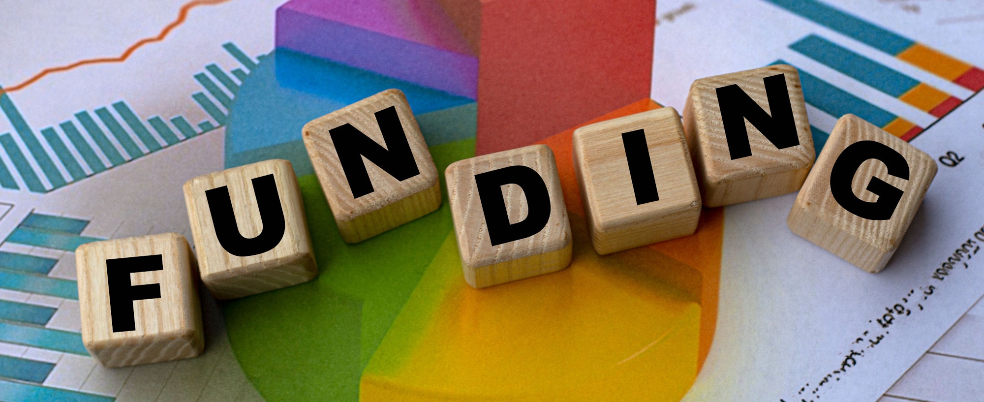 Wooden blocks spelling "FUNDING" on colorful graphs and charts.