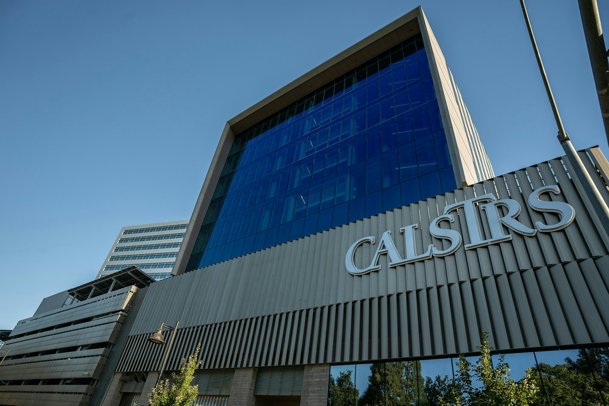 Modern building with "CALSTRS" sign, blue glass facade, under clear sky.
