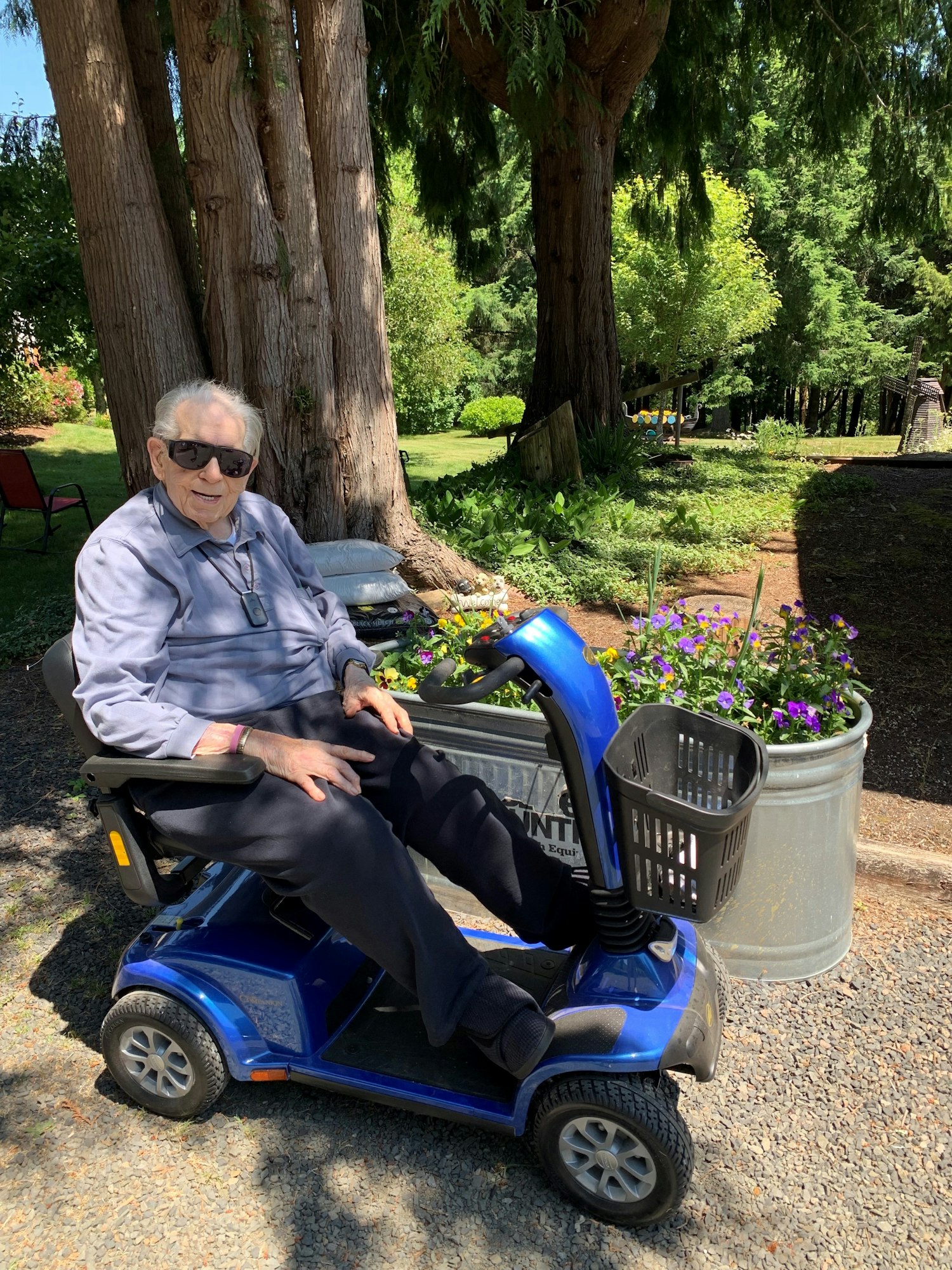 Myron Nelson is in his garden with a mobility scooter. He has white hair and is wearing sunglasses and a blue shirt.