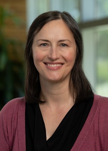 Melissa Jones-Ferguson is wearing a black shirt and maroon cardigan, with a blurred indoor background.