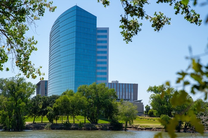 CalSTRS Headquarters by the Sacramento River, surrounded by trees under a clear blue sky.